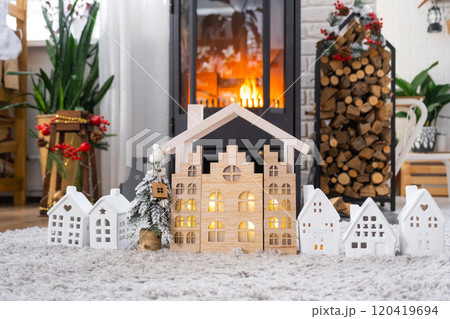 Key on Christmas tree and tiny house on cozy home with Christmas decor near the burning stove fireplace. Gift for New Year. Insurance, moving to new house, mortgage, rent and real estate 120419694