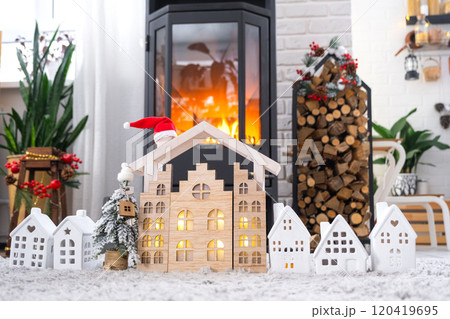 Key on Christmas tree and tiny house on cozy home with Christmas decor near the burning stove fireplace. Gift for New Year. Insurance, moving to new house, mortgage, rent and real estate 120419695