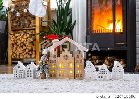 Key on Christmas tree and tiny house on cozy home with Christmas decor near the burning stove fireplace. Gift for New Year. Insurance, moving to new house, mortgage, rent and real estate 120419696