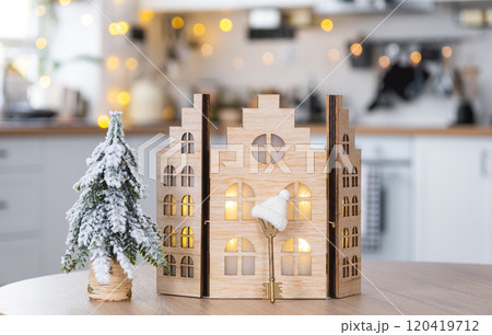 Key on Christmas tree and tiny house on cozy home with Christmas decor on table of festive white kitchen. Gift for New Year. Insurance, moving to new house, mortgage, rent and purchase real estate 120419712
