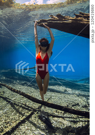 Woman free diver posing underwater with sunken logs at the bottom of the lake. Freediving in crystal-clear lake 120419860