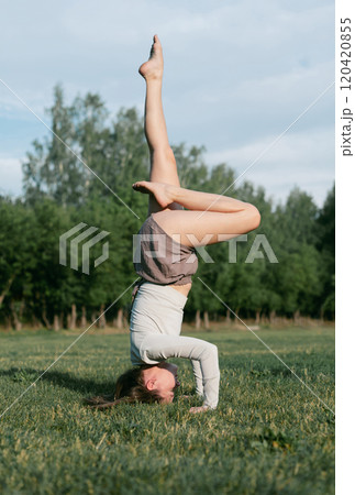 Adult female practising yoga outside on a grass 120420855