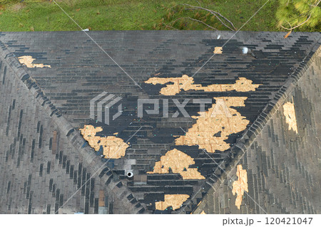 Wind damaged house roof with missing asphalt shingles after hurricane Ian in Florida. Repair of home rooftop concept 120421047