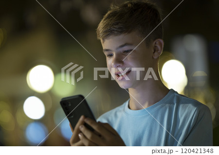 Teenager boy browsing social media on his cellphone on evening street 120421348