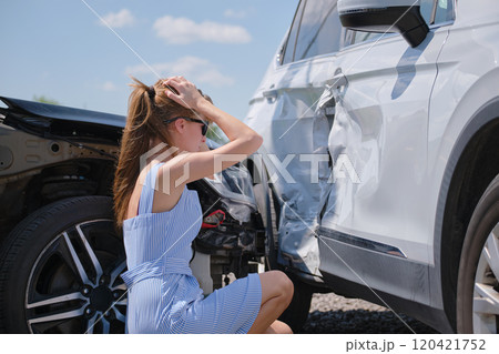 Sad young woman driver sitting near her smashed car looking shocked on crashed vehicles in road accident Sad young woman driver sitting near her smashed car looking shocked on crashed vehicles in road accident 120421752