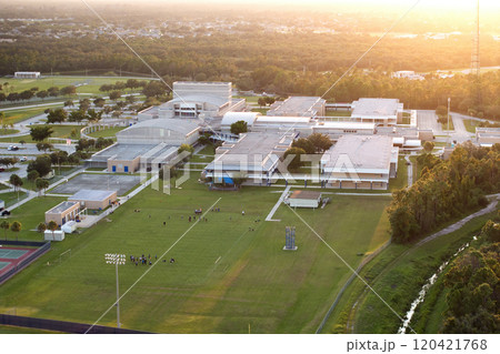 Public school in USA with school kids playing American football game on campus sports stadium at sunset. Physical exercise education in the United States 120421768