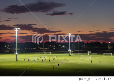 Illuminated public sports arena in North Port, Florida with people playing soccer game on grass football stadium at sunset. Outdoor activities concept 120421947