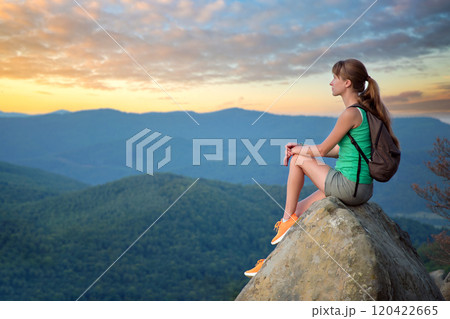 Hiker girl resting on rocky mountain top enjoying morning nature during her travel on wilderness trail. Lonely female traveler traversing high hilltop route. Healthy lifestyle concept 120422665