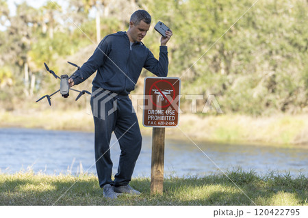 Drone operator is disappointed because he isn't allowed to fly his quadcopter in national park no drone area. Man is unable to use his UAV near restriction notice sign. Airspace use regulations 120422795
