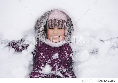 A little girl in winter clothing smiles joyfully while surrounded by deep snow, capturing the magic of a snowy winter day 120423305