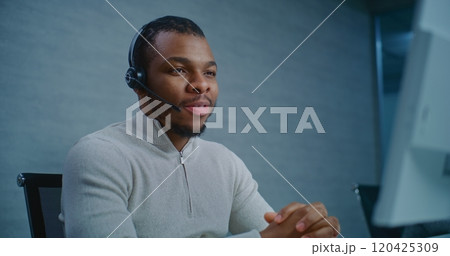 African American hotline operator talking on headset with customer, providing online assistance 120425309