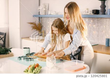 Family preparation of ginger biscuits with daughter. Mother and little girl cooking cookies. Blonde woman wearing blue shirt and girl white t-shirt. 120425801