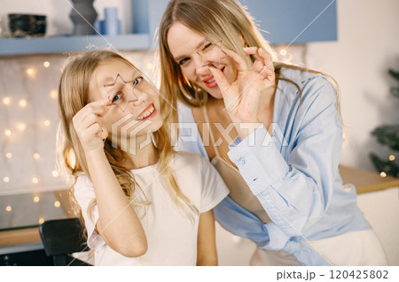 Blonde woman and her daughter holding a cookie cutters. Family preparation of ginger biscuits with child. Mother and daughter cooking cookies. 120425802