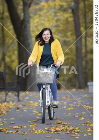Happy middle aged woman rides a bicycle in the autumn park. Happy middle aged woman rides a bicycle in the autumn park. 120426832