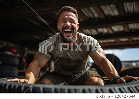 Smiling man in sportswear lifting large car tires in the gym. Smiling man in sportswear lifting large car tires in the gym. 120427044