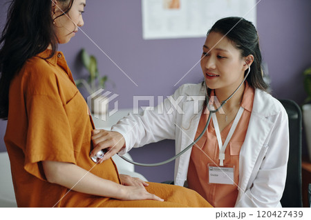 Doctor Examining Pregnant Patient with Stethoscope in Office Doctor Examining Pregnant Patient with Stethoscope in Office 120427439