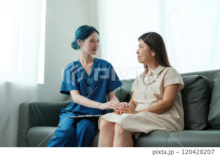 A woman in a blue scrubs sits on a couch with a woman in a white dress A woman in a blue scrubs sits on a couch with a woman in a white dress 120428207