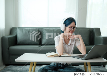 A woman wearing headphones and glasses is sitting at a table with a laptop A woman wearing headphones and glasses is sitting at a table with a laptop 120428227