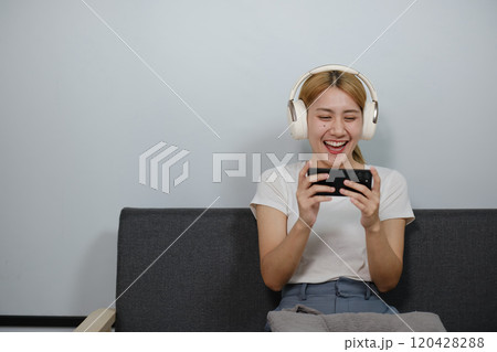 A woman is sitting on a couch and playing a game on her phone A woman is sitting on a couch and playing a game on her phone 120428288