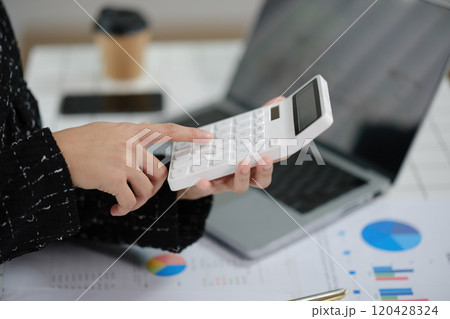 A person is using a calculator on a laptop while looking at a graph A person is using a calculator on a laptop while looking at a graph 120428324