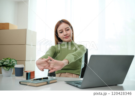A woman is sitting at a desk with a laptop and a notebook 120428346