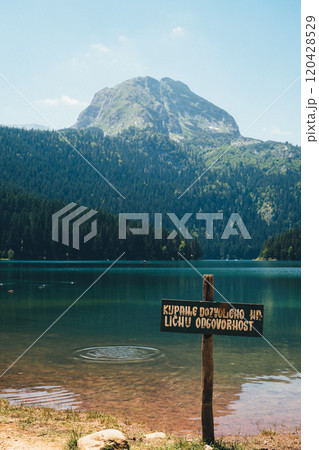 Serene lake view with a wooden sign near a mountain in a tranquil setting during daytime 120428529