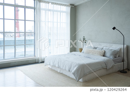 Stylish loft bedroom interior. Spacious design apartment with light walls large windows big bed. Clean modern decoration with elegant furniture in minimalist Scandinavian style 120429264
