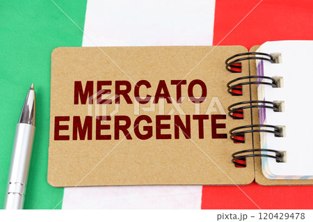 On the flag of Italy lies a pen and a notebook with the inscription - emerging market On the flag of Italy lies a pen and a notebook with the inscription - emerging market 120429478
