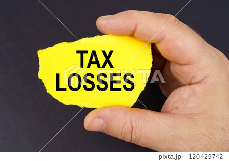 On a black background, in the hands of a man, a yellow torn cardboard with the inscription - tax losses 120429742