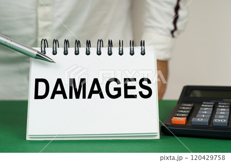 On a green surface, a calculator and a notepad with the inscription - damages On a green surface, a calculator and a notepad with the inscription - damages 120429758
