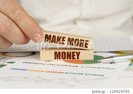 On the table are business charts and diagrams in the hands of a wooden block with the inscription - Make More Money 120429792