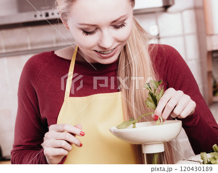 Woman in kitchen making vegetable smoothie juice 120430189