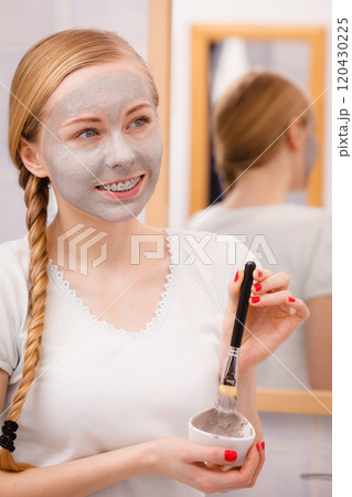 Woman applying with brush clay mud mask to her face 120430225