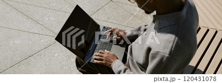 Man using laptop on bench outdoors on sunny day, focusing on work. Laptop screen capturing sunlight reflections, creating productive work environment 120431078