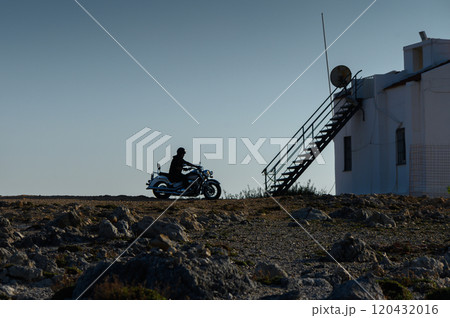 Riding into serenity: A lone motorcyclist approaches a remote building at dusk. Riding into serenity: A lone motorcyclist approaches a remote building at dusk. 120432016