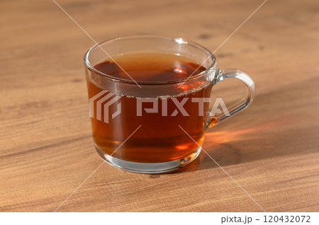 A cozy glass of freshly brewed tea resting on a wooden table in the warm afternoon sunlight 120432072