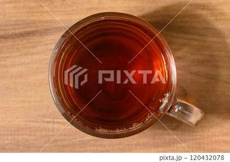 A warm cup of brewed tea resting on a wooden table in a cozy setting A warm cup of brewed tea resting on a wooden table in a cozy setting 120432078
