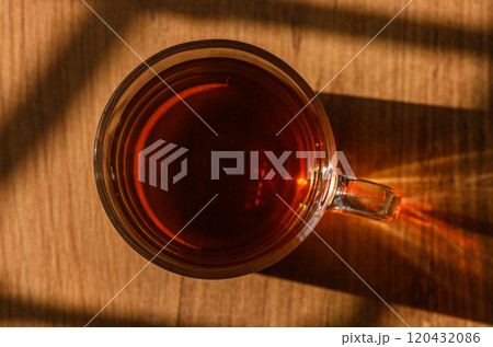 Warm cup of tea rests on a wooden table, basking in soft afternoon sunlight 120432086