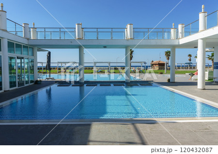 A serene swimming pool with ocean views at a luxurious beachfront resort under a clear blue sky. 120432087