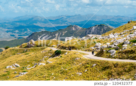 A scenic mountain road winding through rocky slopes with expansive views of valleys and distant ridges, perfect for adventurers and nature lovers. 120432377