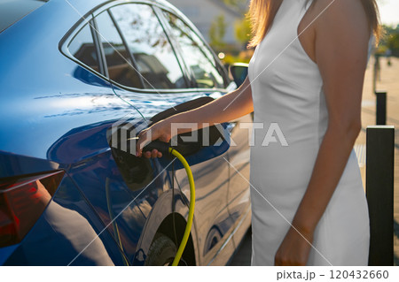 Close up woman in a white dress connecting an electric car to a charging station on a city street Close up woman in a white dress connecting an electric car to a charging station on a city street 120432660