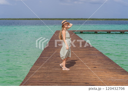 Female tourist in a turquoise dress standing on a wooden pier over the turquoise waters of Bacalar Lake, Mexico. Peaceful tropical travel destination concept 120432706