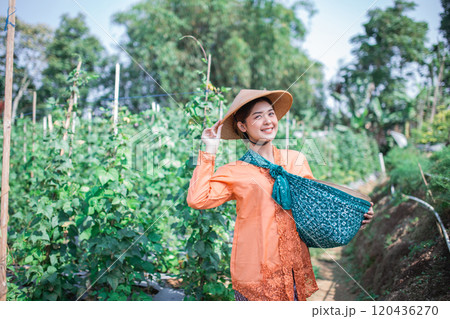 A Smiling Woman Surrounded by a Vibrantly Colorful Vegetable Garden While Holding a Basket 120436270