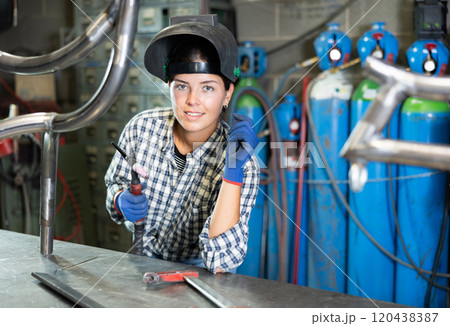 Portrait of a female welder standing with a welding machine and a safety helmet in metal machining workshop Portrait of a female welder standing with a welding machine and a safety helmet in metal machining workshop 120438387
