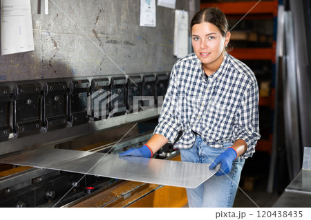 Female worker operating metal press brake in workshop Female worker operating metal press brake in workshop 120438435