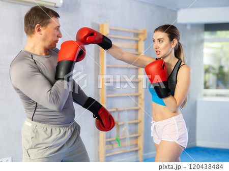 Woman and man in sportswear are engaged in boxing sparring in gym Woman and man in sportswear are engaged in boxing sparring in gym 120438484
