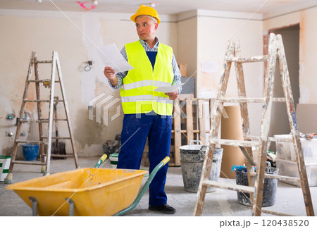 Portrait of worker in a yellow vest with documents in his hands in renovated cottage 120438520