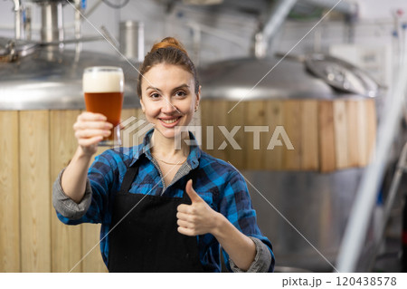 Female brewer showing thumbs up while holding glass of beer 120438578