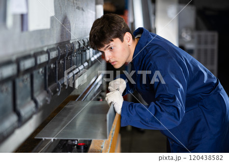 Young worker operating metal press brake in industrial workshop 120438582