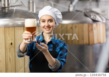 Portrait of female brewer who is standing with glass of beer on his workplace in brew-house Portrait of female brewer who is standing with glass of beer on his workplace in brew-house 120438756